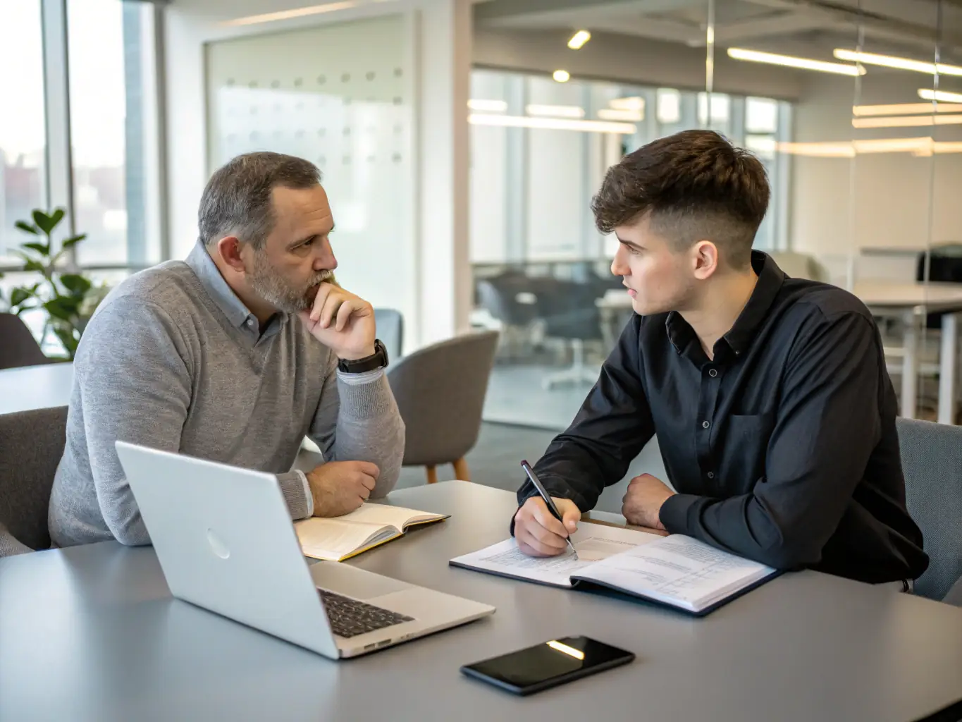 An image of a mentor and mentee discussing business plans over a laptop in a professional environment, representing mentoring for business growth.